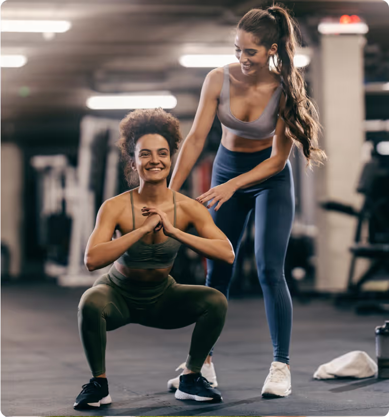 personal trainer helps client do the squat in a gym